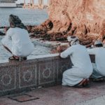 arab men in white traditional wear praying on embankment