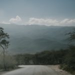 asphalt roadway through green plants towards hills