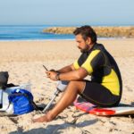 focused ethnic sportsman with leg prosthesis using smartphone on beach